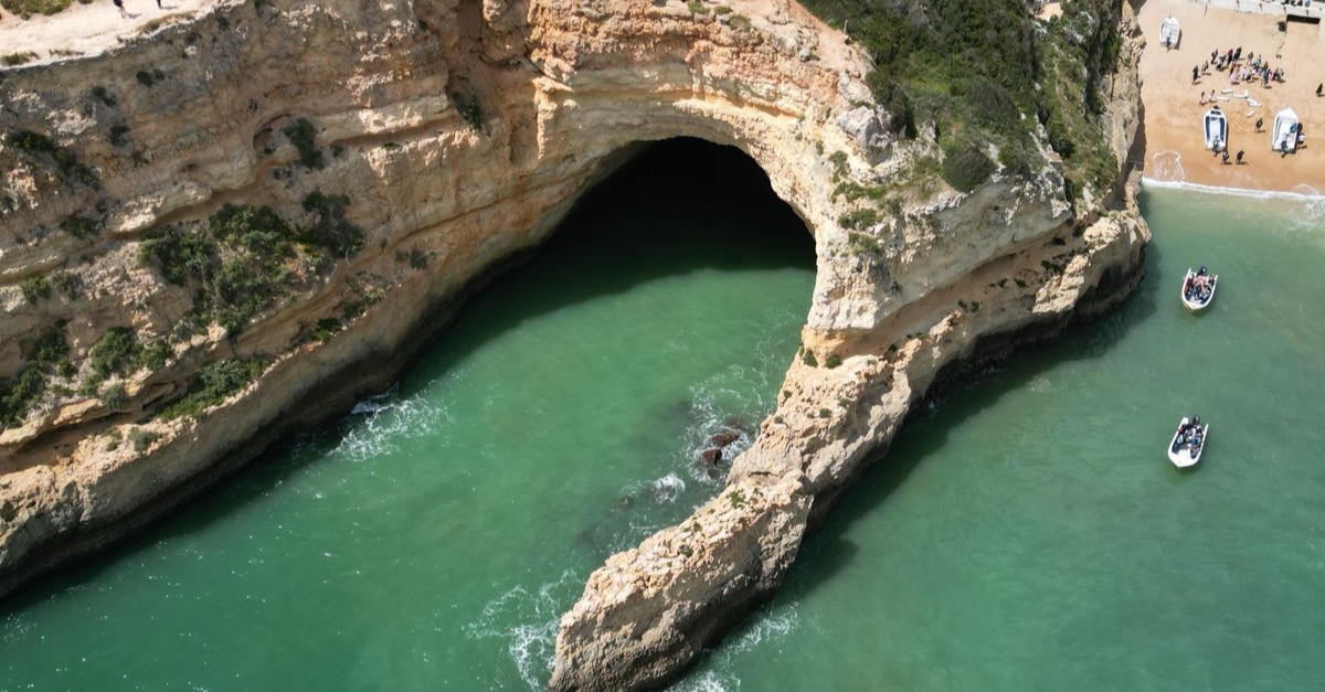 Aerial view of the Algar de Benagil rock arch with two inflatable boats on turquoise water