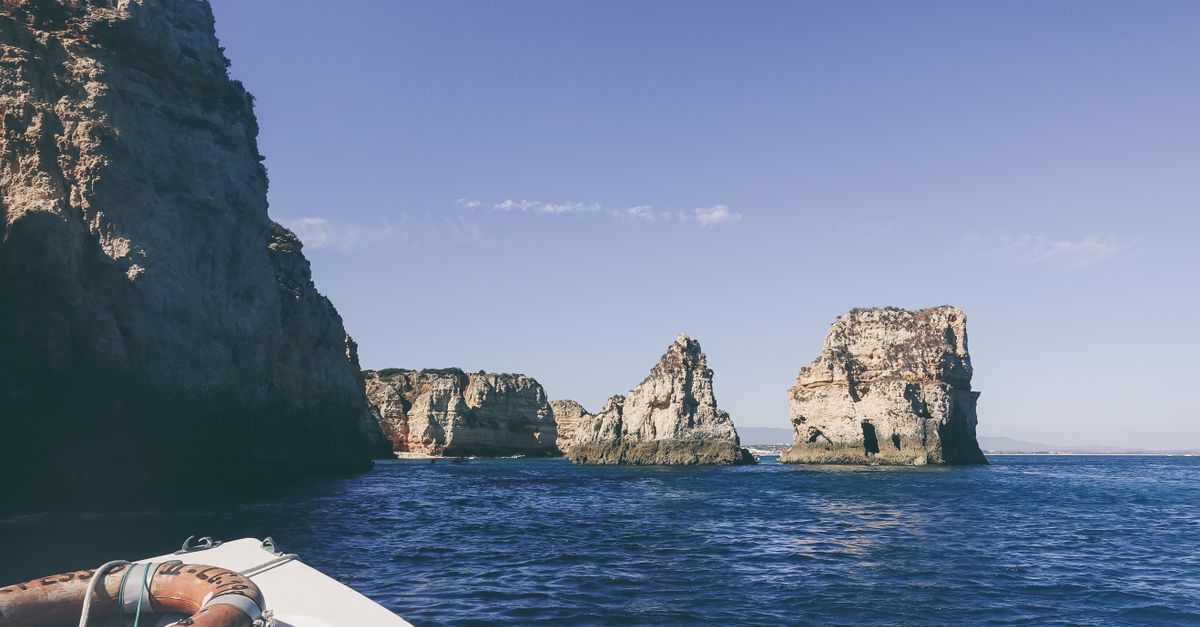 View from the bow of a tour boat towards limestone rock stacks and calm water on the Algarve coast, life ring in the foreground