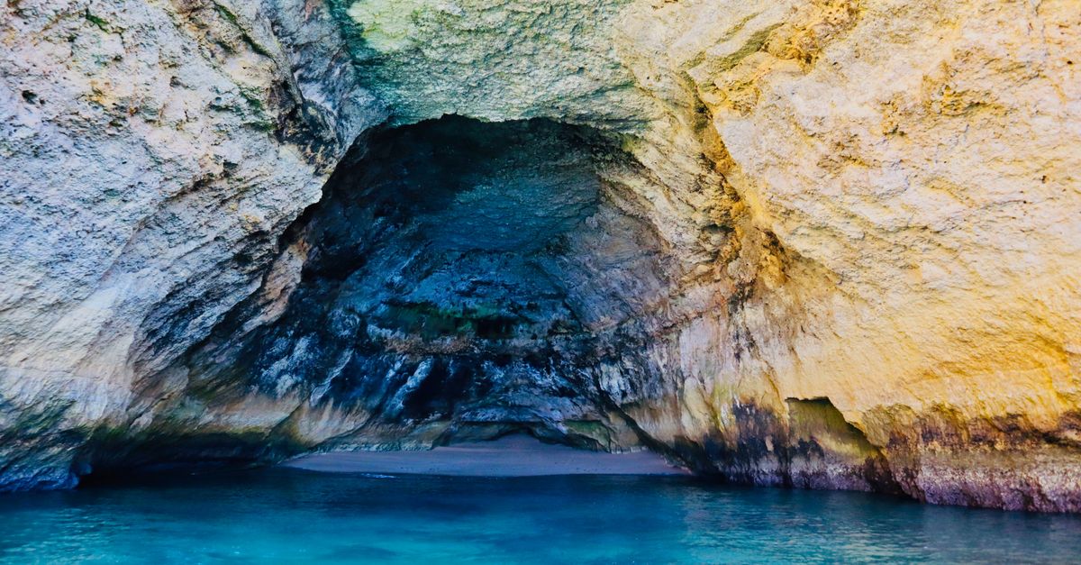 View from the water into a sea cave with a small sandy beach and turquoise water near Carvoeiro on the Algarve