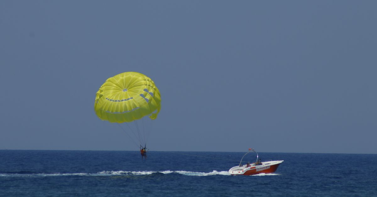 Yellow parasail canopy with one person in the harness, towed by a motorboat over open sea
