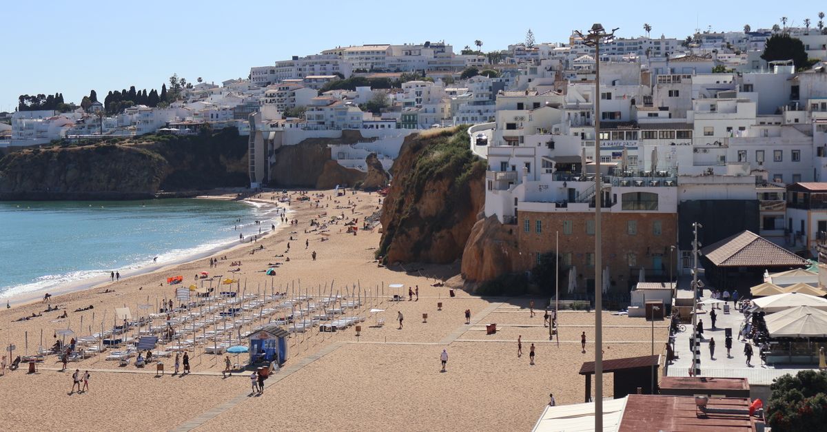 Albufeira’s town beach with rows of sunbeds and reddish rocks, with the white houses of the old town on the hillside above