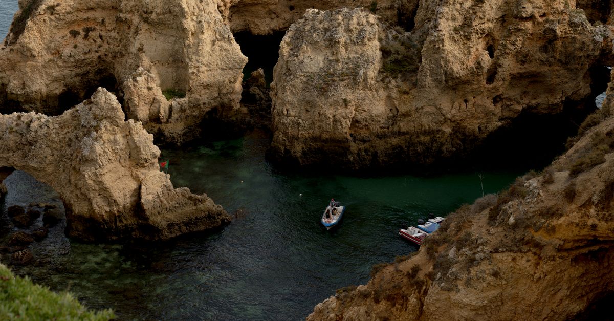 Small boats in a green bay between golden limestone cliffs and caves on the Algarve coast, seen from the clifftop