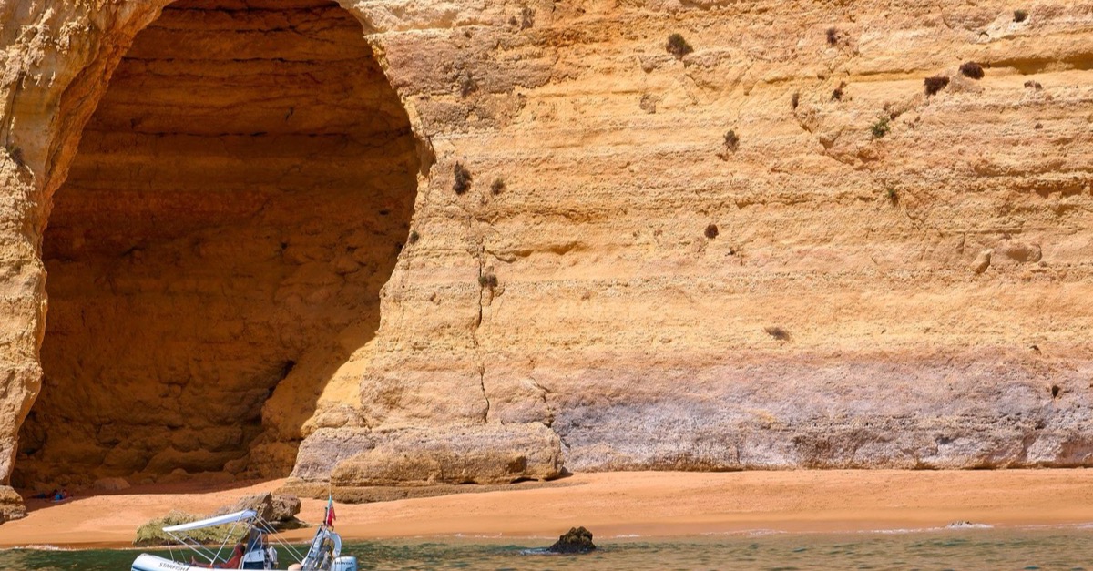 A small excursion boat in front of the tall rock arch of a sea cave on the Algarve coast